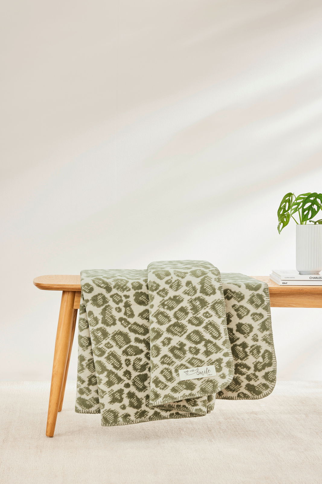 Grüne Wohndecke mit Leopardenmuster, drapiert über einer Holzbank, seitliche Perspektive.
