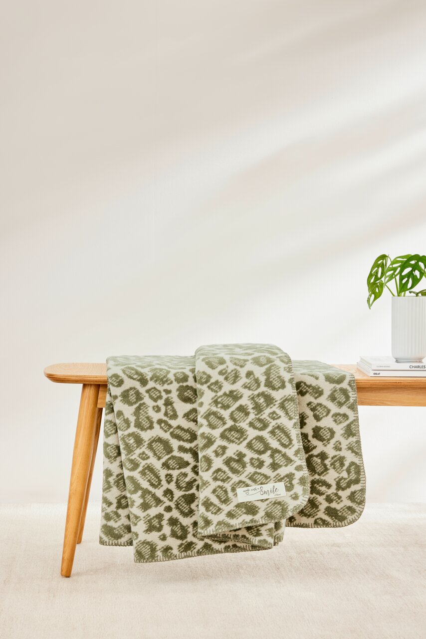 Groene deken met luipaardprint, gedrapeerd over een houten bank, zijaanzicht.