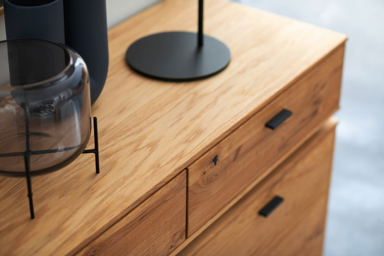Nahaufnahme eines Sideboards aus Holz mit modernen schwarzen Griffen und Dekorationen auf der Oberseite, aus schräger Perspektive fotografiert.