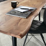 Nahaufnahme eines Esstisches aus Holz mit natürlicher Kante, darauf liegen ein Notizbuch, ein Stift und eine Tasse, seitliche Perspektive