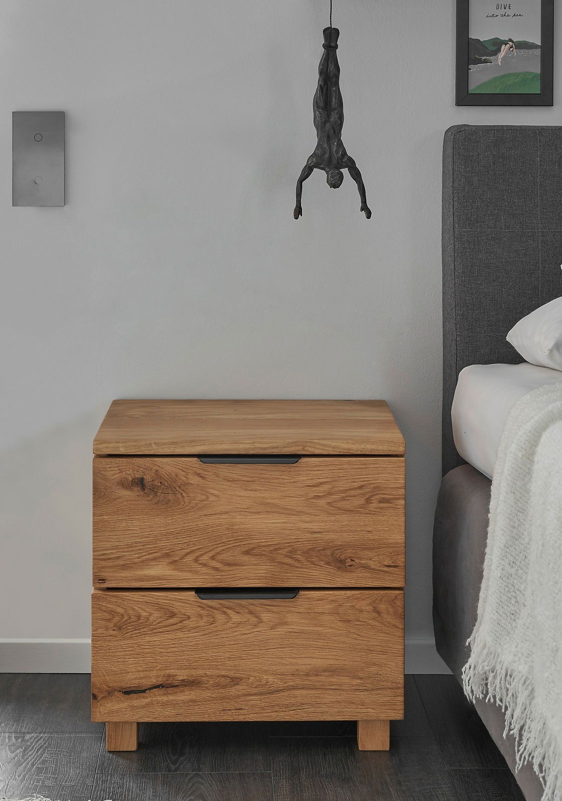 Holz-Nachtkommode mit zwei Schubladen, frontal fotografiert, neben einem Bett.