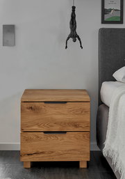 Holz-Nachtkommode mit zwei Schubladen, frontal fotografiert, neben einem Bett.