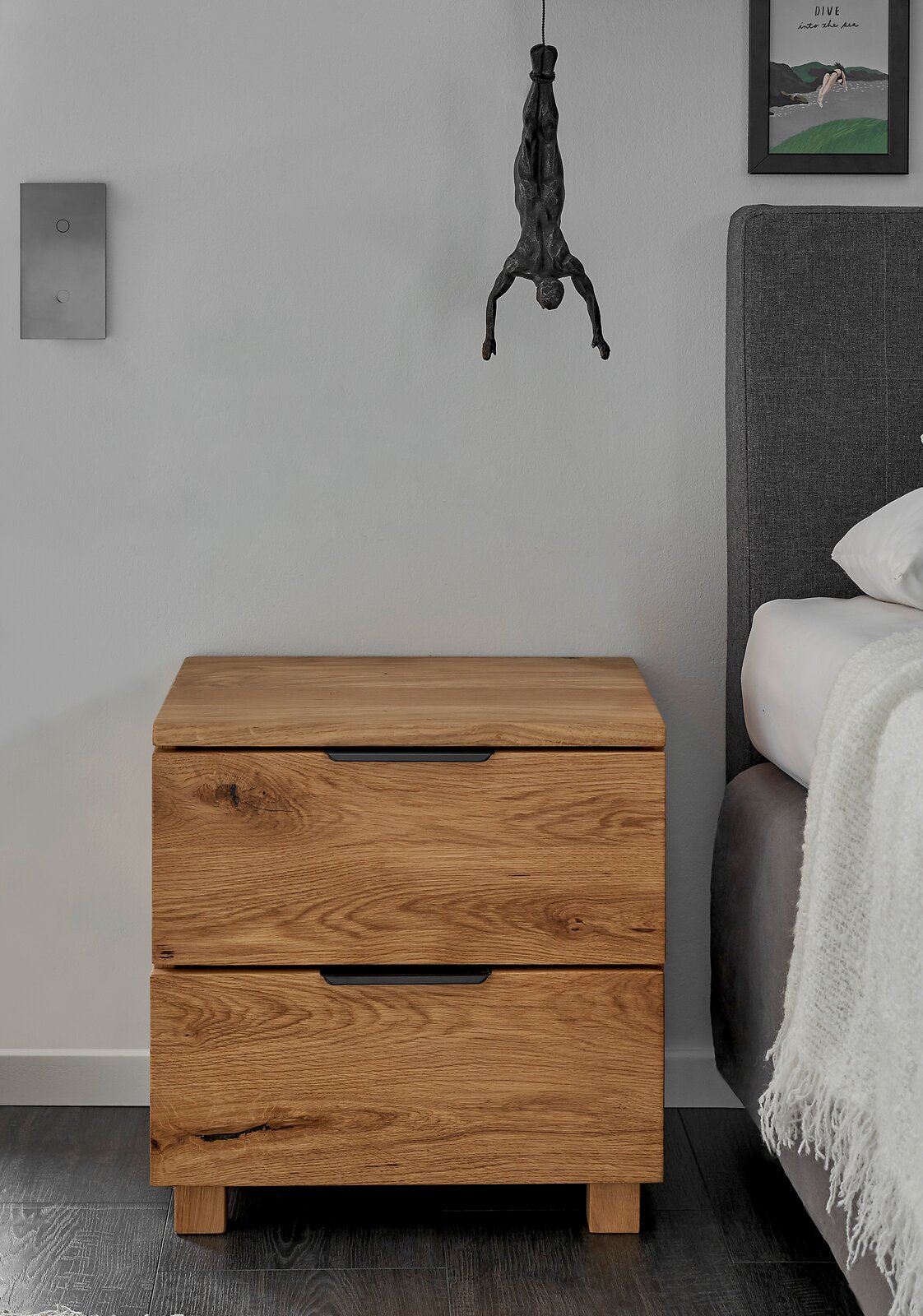 Holz-Nachtkommode mit zwei Schubladen, frontal fotografiert, neben einem Bett.