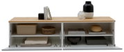 Frontale Ansicht eines modernen Sideboards/Lowboards mit heller Holzplatte und weißen Klapptüren, geöffnet und mit Deko sowie Aufbewahrungsboxen in den Fächern, auf weißem Hintergrund.