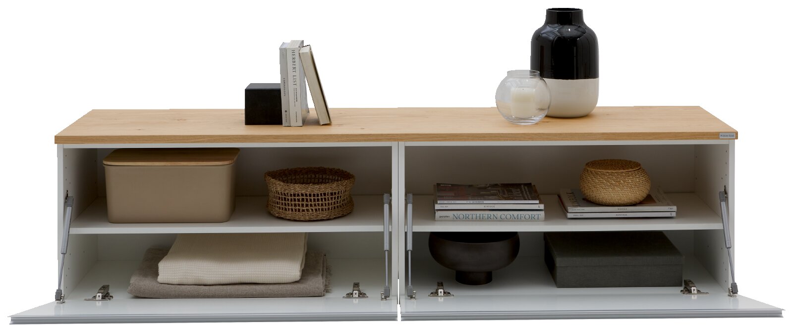 Frontale Ansicht eines modernen Sideboards/Lowboards mit heller Holzplatte und weißen Klapptüren, geöffnet und mit Deko sowie Aufbewahrungsboxen in den Fächern, auf weißem Hintergrund.
