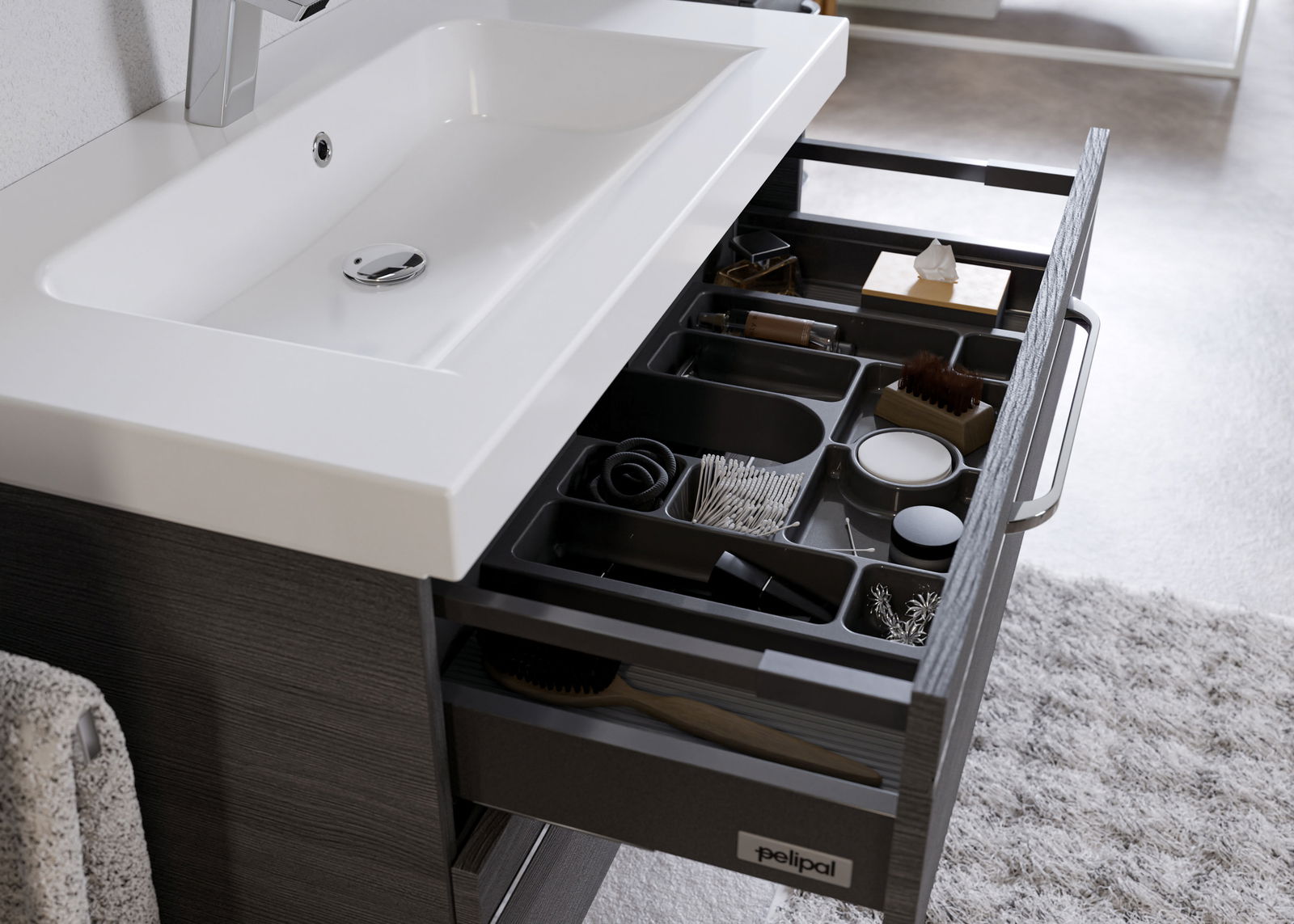 Moderner Badblock mit weißem Waschbecken und geöffneter Schublade, die verschiedene Pflegeprodukte und Accessoires zeigt, aus der Perspektive von oben.
