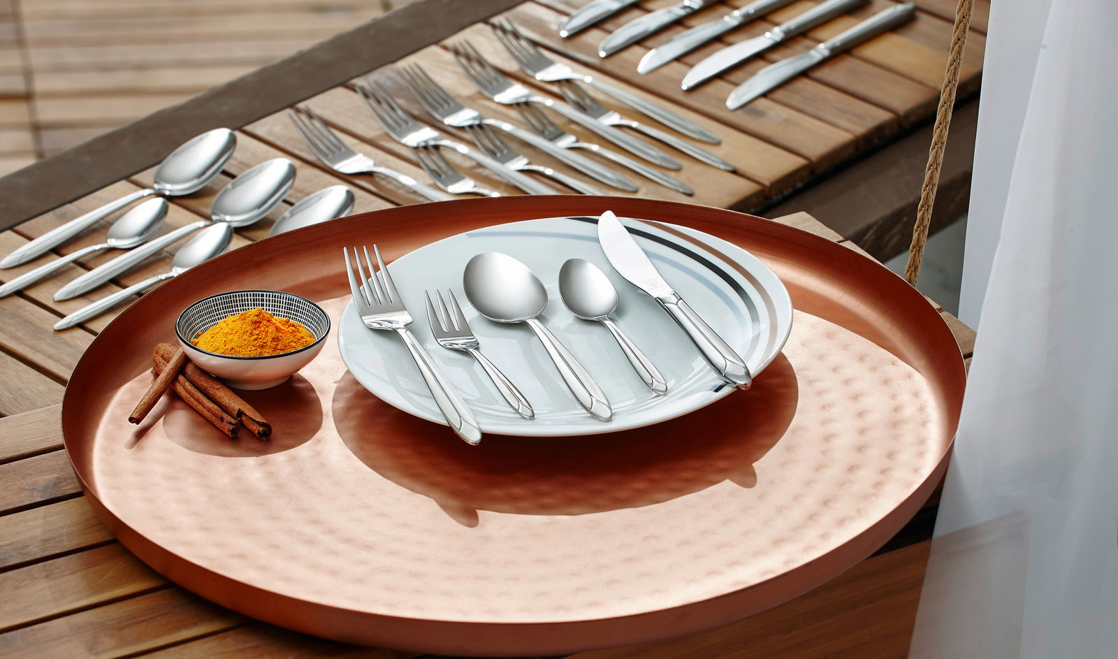 Ein 60-teiliges Besteckset 'Classic' auf einem Tisch, präsentiert auf einem Teller mit einem Kupfertablett. Perspektive von oben.