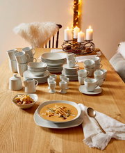 Ein 62-teiliges Kombiservice auf einem Holztisch, bestehend aus Tellern, Tassen und Schalen, mit einer gemütlichen Tischdekoration und Kerzen im Hintergrund. Perspektive von oben.
