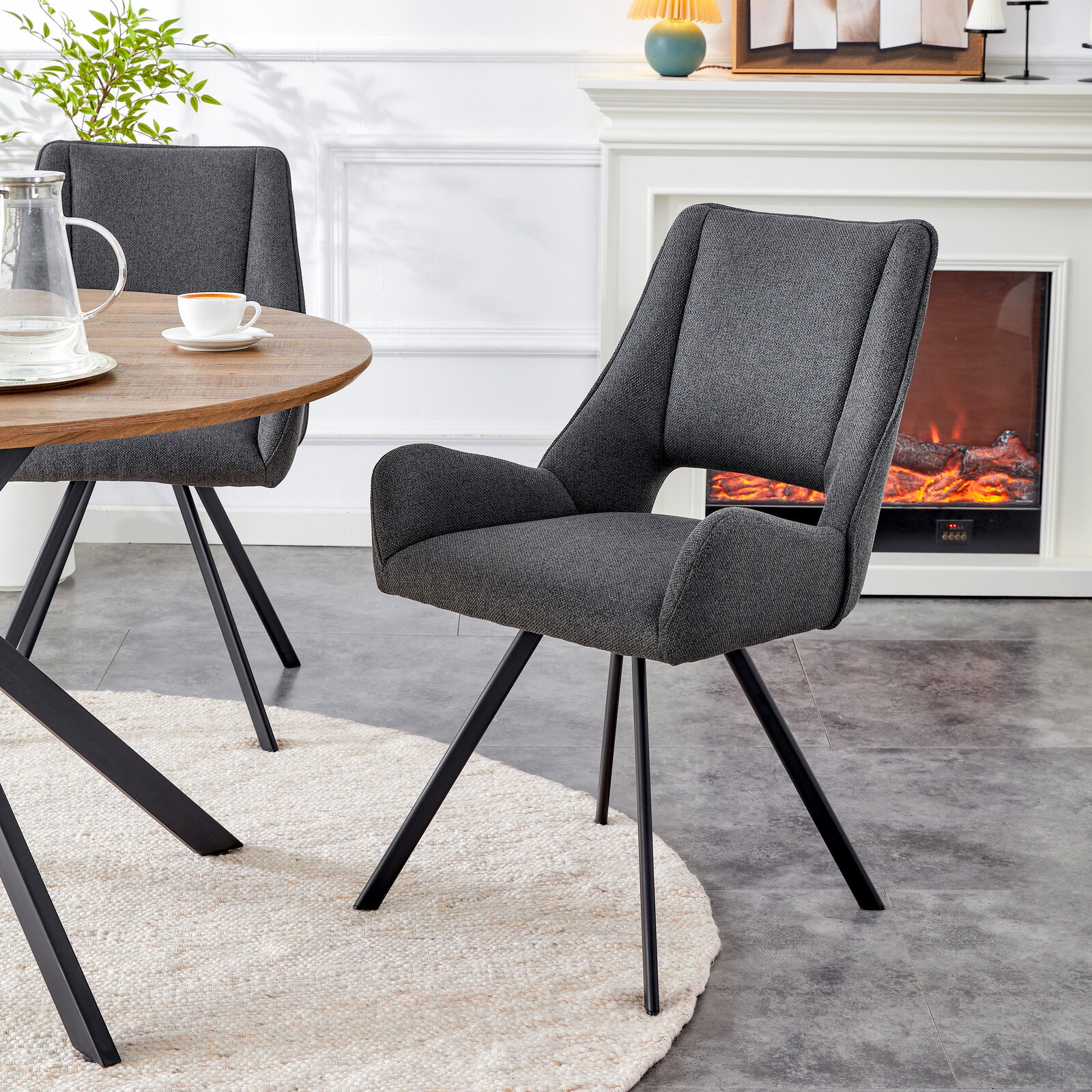 Dunkelgrauer, gepolsterter Polsterstuhl mit Armlehnen und schwarzen Metallbeinen am Esstisch im Wohnzimmer, seitliche Frontansicht (3/4-Perspektive)