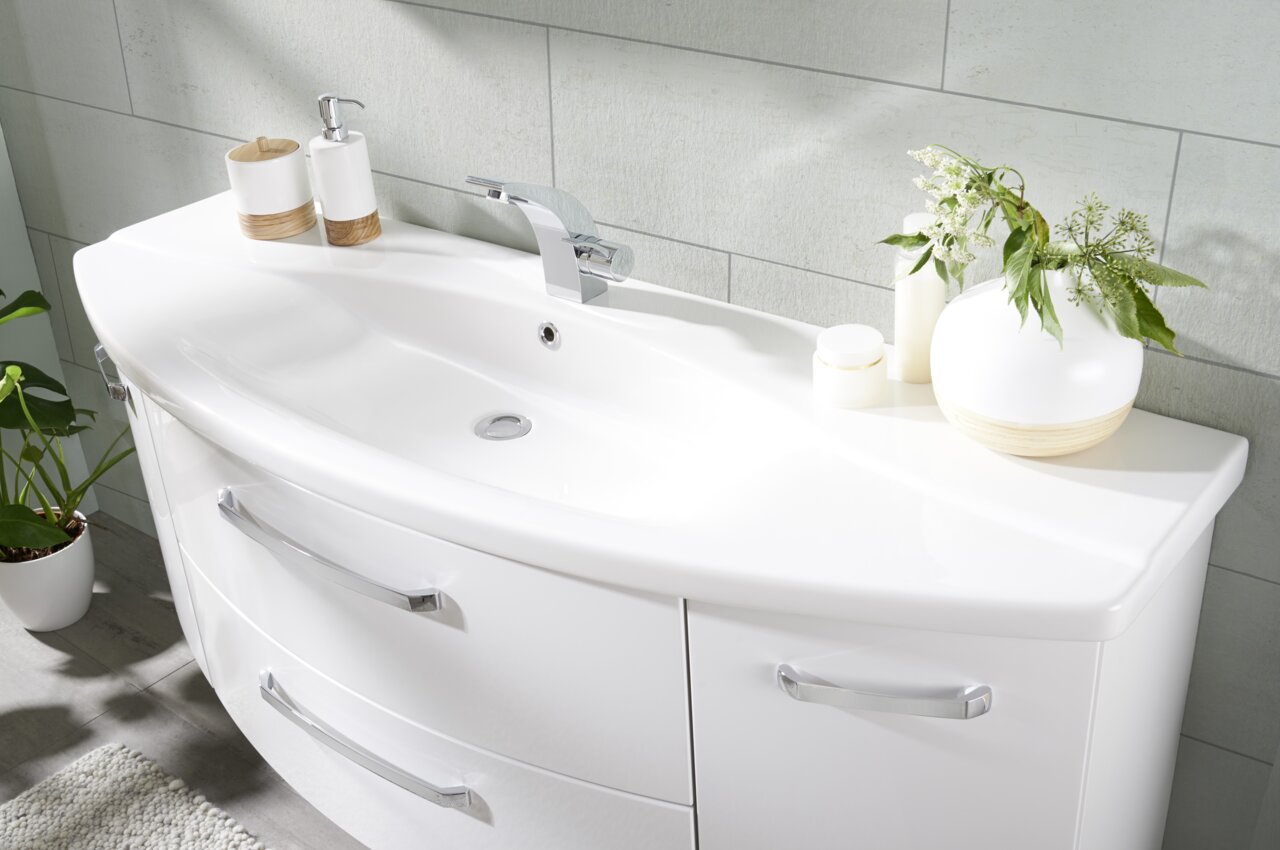 Moderne Badkombination mit weißem Waschbecken und Unterschrank, dekoriert mit Pflanzen und Accessoires, aus seitlicher Perspektive fotografiert.