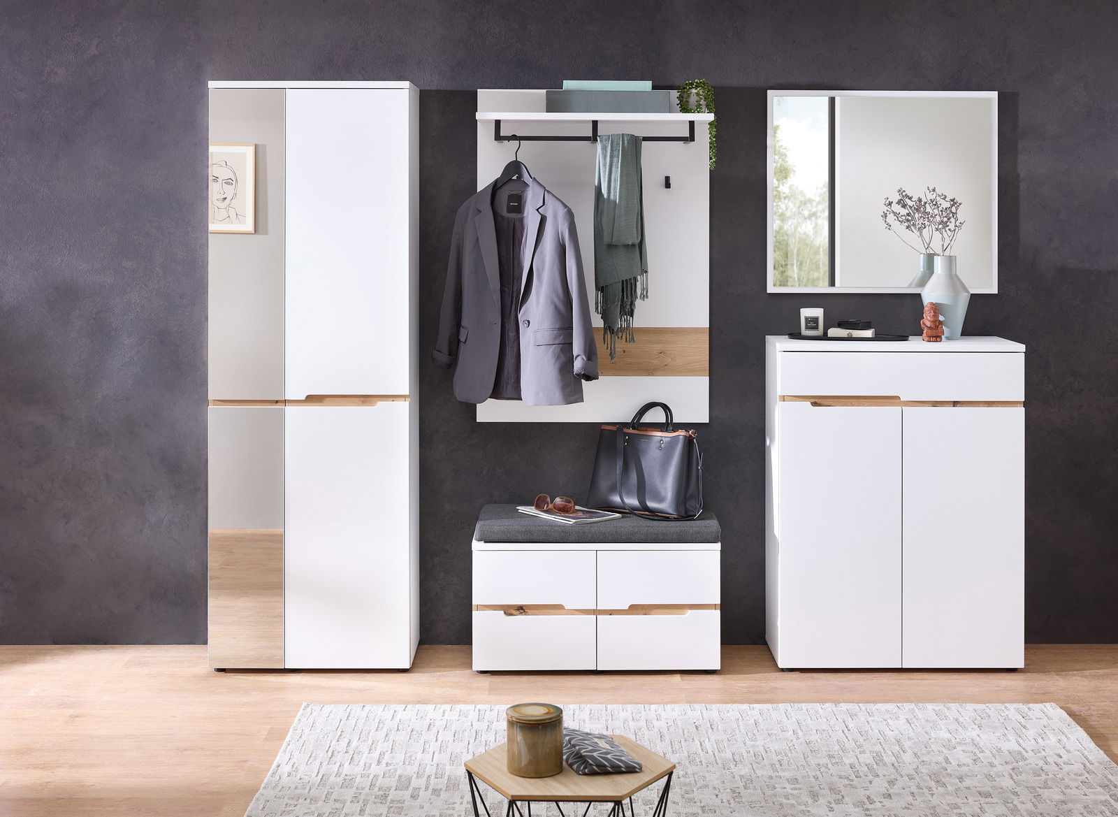 Moderne Garderobenset in Weiß mit Holzdetails, bestehend aus einem hohen Schrank, einem Garderobenpaneel mit Haken und Ablage, einer Sitzbank mit Stauraum und einem Spiegel. Frontalansicht.