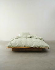 Minimalistisches Schlafzimmer mit einem niedrigen Holzbett, bezogen mit hellgrüner Bettwäsche, aus der Vorderansicht fotografiert.