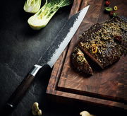 Kiritsuke-Messer KYOTO 23 cm mit gehämmerter Klinge und dunklem Holzgriff, auf einem Schneidebrett neben geschnittenem Fleisch und Gemüse, aus der Vogelperspektive.