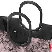 Nahaufnahme einer stilvollen Einkaufstasche mit schwarzen, ovalen Griffen und einem rosa-weißen Baum-Muster. Die Tasche hat einen Reißverschluss und das Bild zeigt die obere Perspektive.