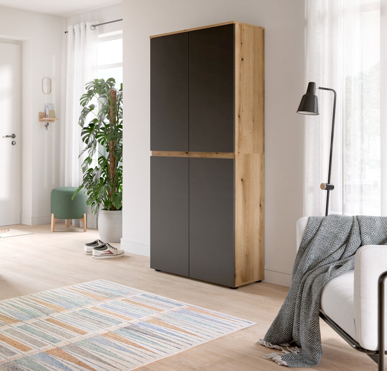 Moderner, hoher Schrank in Eiche-Optik mit mattschwarzen Fronten im hellen Wohnzimmer, perspektivisch in leichter Seitenansicht von vorn fotografiert.