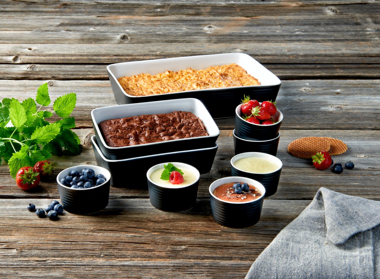 Set van 9 bakvormen met diverse desserts en fruit, van bovenaf gezien, gerangschikt op een houten tafel.