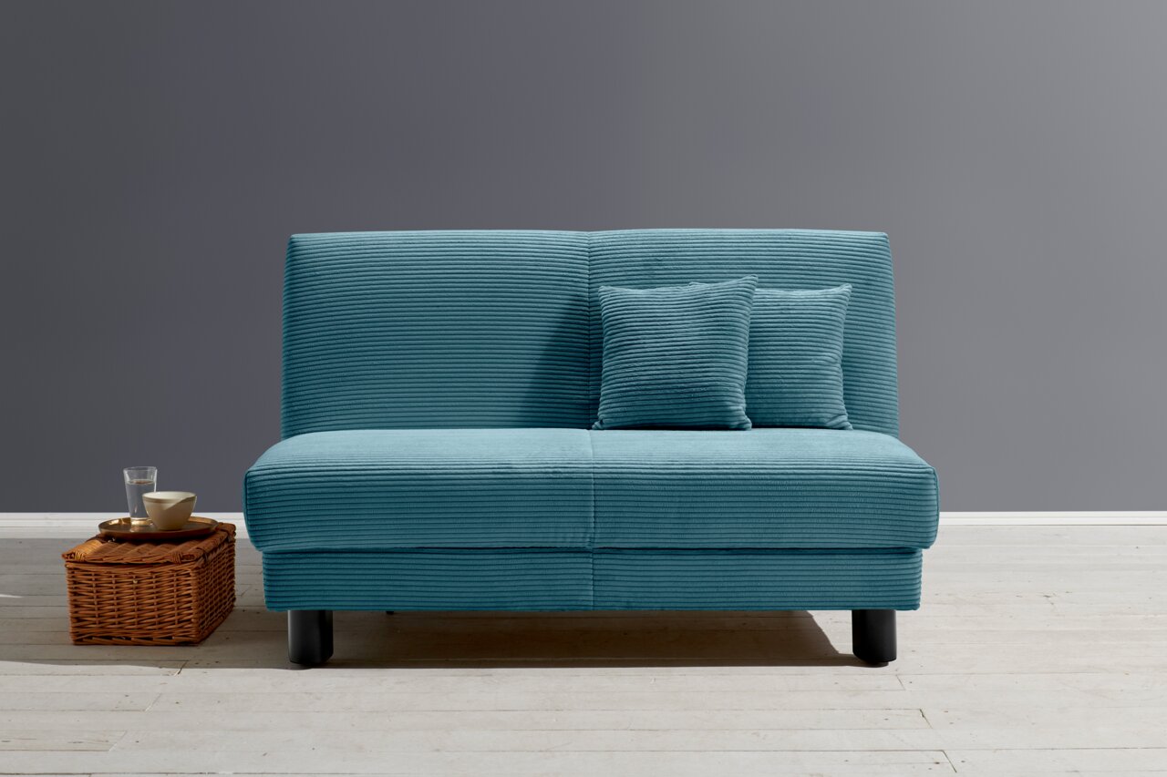 Z2 Schlafsofa ENNY Blaues Funktionssofa ENNY mit zwei Kissen, frontal fotografiert, auf hellem Holzboden vor grauer Wand.