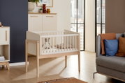 Anstellbett aus Holz mit weißen Gitterstäben in einem modernen Wohnzimmer, seitliche Perspektive