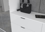 Weiße Kommode mit zwei Schubladen, darauf eine schwarze Handtasche und eine Brille, seitliche Perspektive
