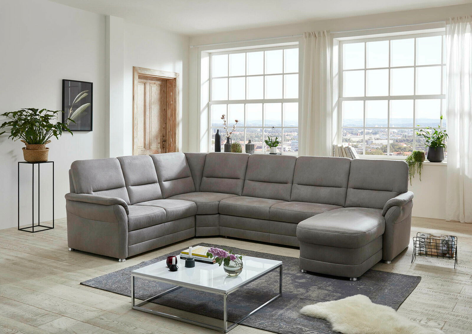 Graue Polsterrundecke in einem modernen Wohnzimmer mit großen Fenstern, von vorne betrachtet.