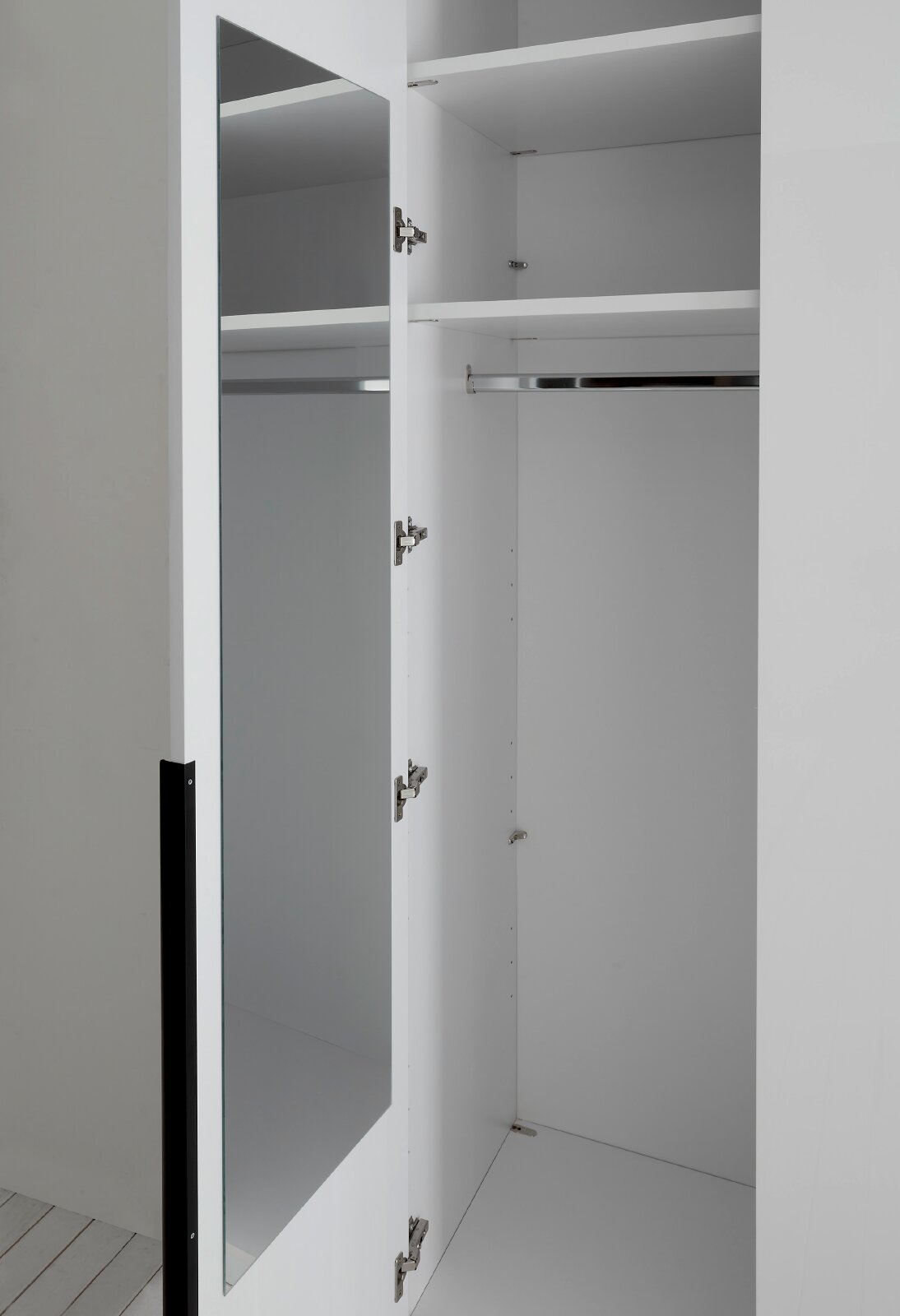 Geöffneter weißer Kleiderschrank mit verspiegelter Tür, Einlegeböden und Kleiderstange, in schräger Nahansicht von vorn