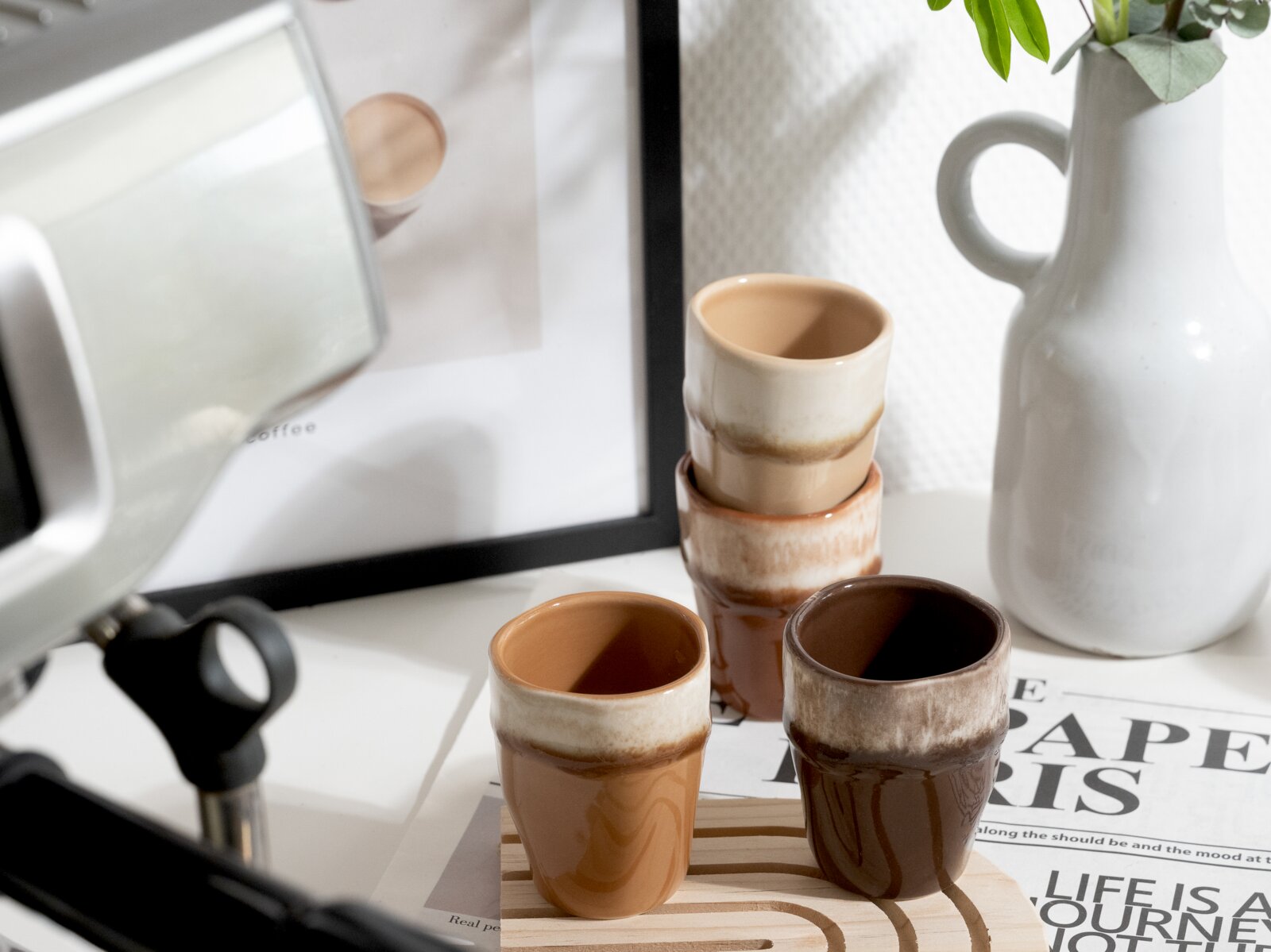 Creatable Espressobecher 4-tlg SQUEEZY Vier kleine, glasiert-keramische Espresso-/Schnapsbecher in Braun- und Cremetönen auf einem hellen Holztablett, fotografiert in leichter Seitenansicht von schräg oben; im Hintergrund eine weiße Kanne und ein gerahmtes Bild.
