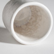 Nahaufnahme einer weiß-beigen, marmorierten Keramikvase/Becher, liegend fotografiert mit Blick in die Öffnung (Frontansicht/Top-Down-Perspektive), auf hellem Hintergrund.