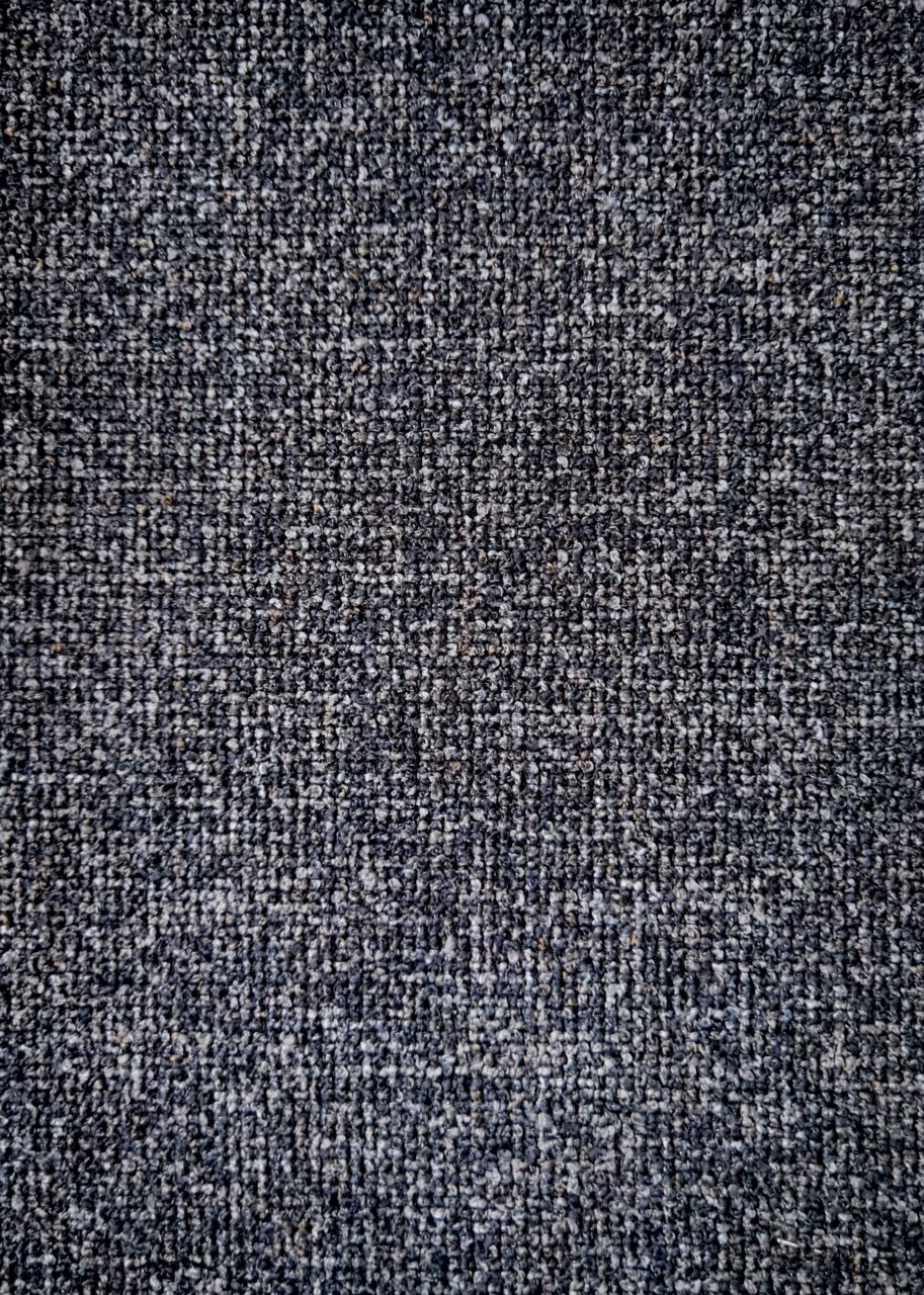 Dieter Knoll Armlehnstuhl PABLO Nahaufnahme eines grauen Stoffmusters, das für einen Armlehnstuhl verwendet wird, von oben betrachtet.