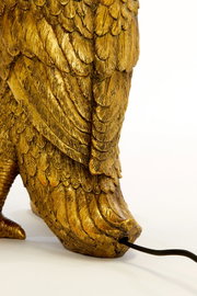 Detailfoto van een gouden tafellamp in de vorm van een vogel, met gedetailleerde veren en een kabel die uit de voet steekt.