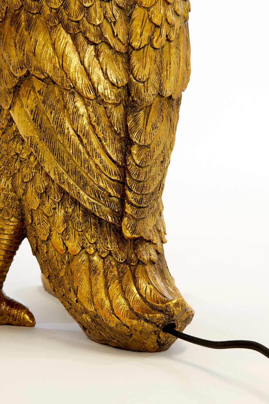 Detailfoto van een gouden tafellamp in de vorm van een vogel, met gedetailleerde veren en een kabel die uit de voet steekt.