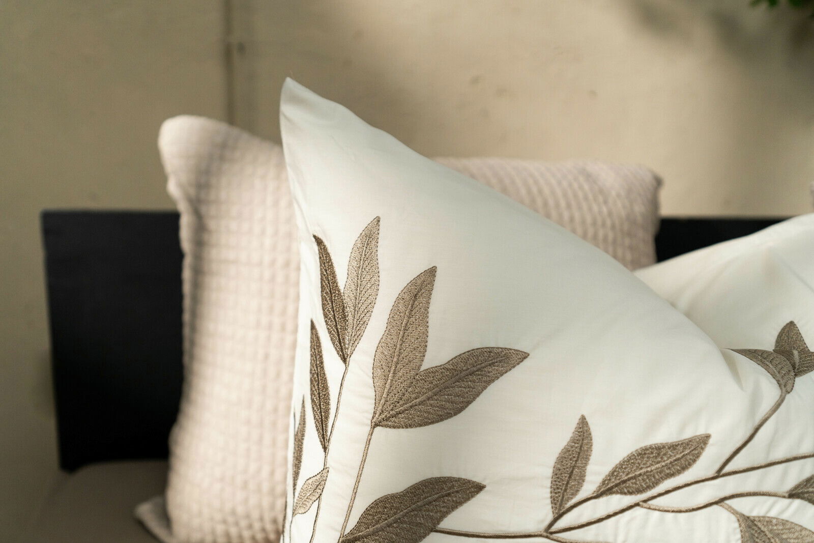 Nahaufnahme eines weißen Kissens mit beigem Blattmuster, im Hintergrund ein weiteres strukturiertes Kissen, seitliche Perspektive.