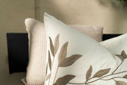 Nahaufnahme eines weißen Kissens mit beigem Blattmuster, im Hintergrund ein weiteres strukturiertes Kissen, seitliche Perspektive.