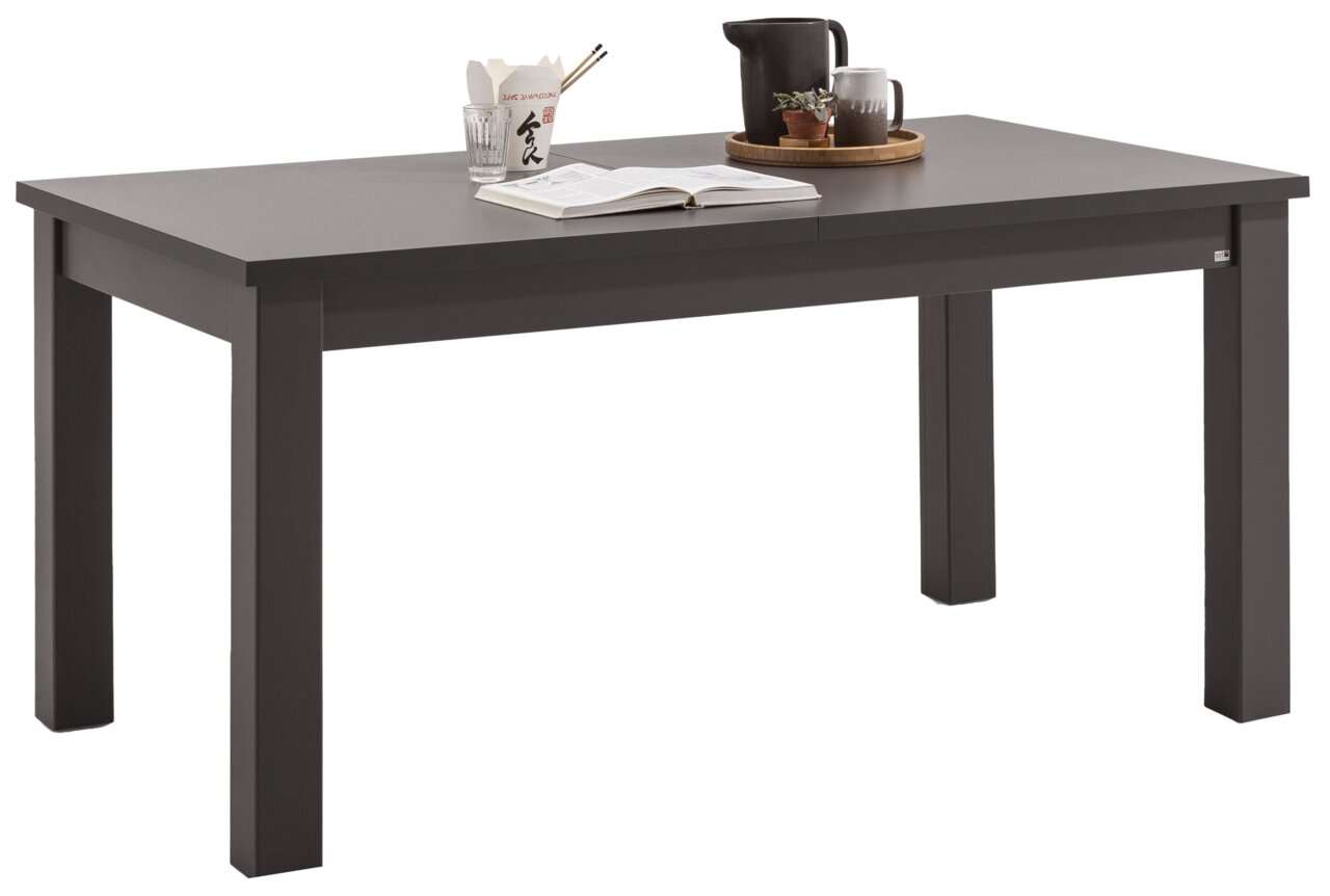 Set one by Musterring Esstisch TACOMA Moderner, ausziehbarer Esstisch in dunkler Farbe, seitliche Perspektive, dekoriert mit Geschirr und Pflanzen.