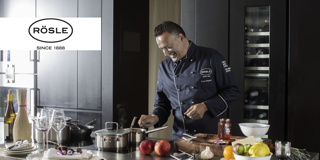 Een kok in een donker uniform bereidt in een moderne keuken een gerecht met verse ingrediënten.