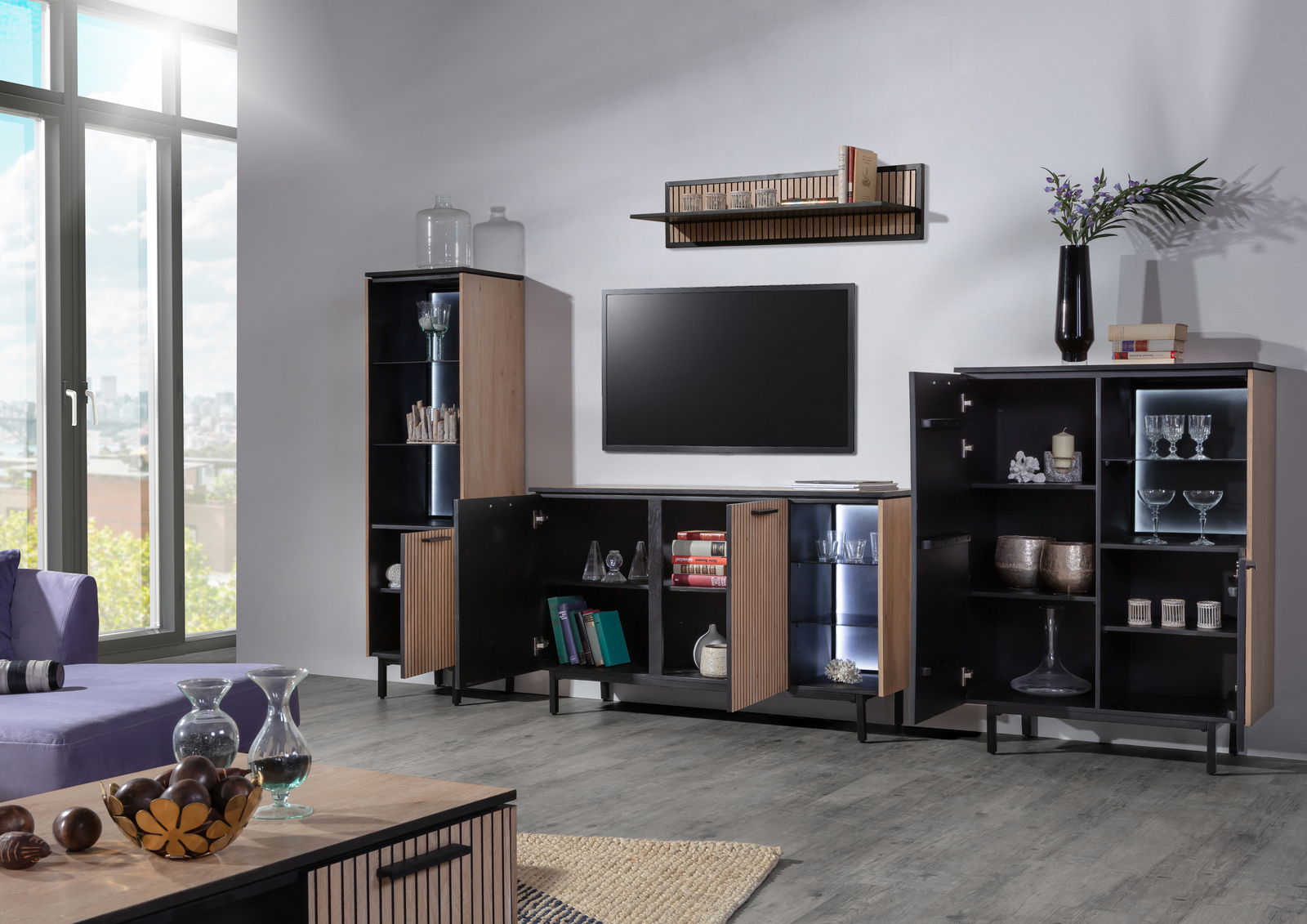 Moderne Wohnzimmermöbel in einem hellen Raum mit TV-Lowboard, Wandboard und Vitrine, seitliche Perspektive.