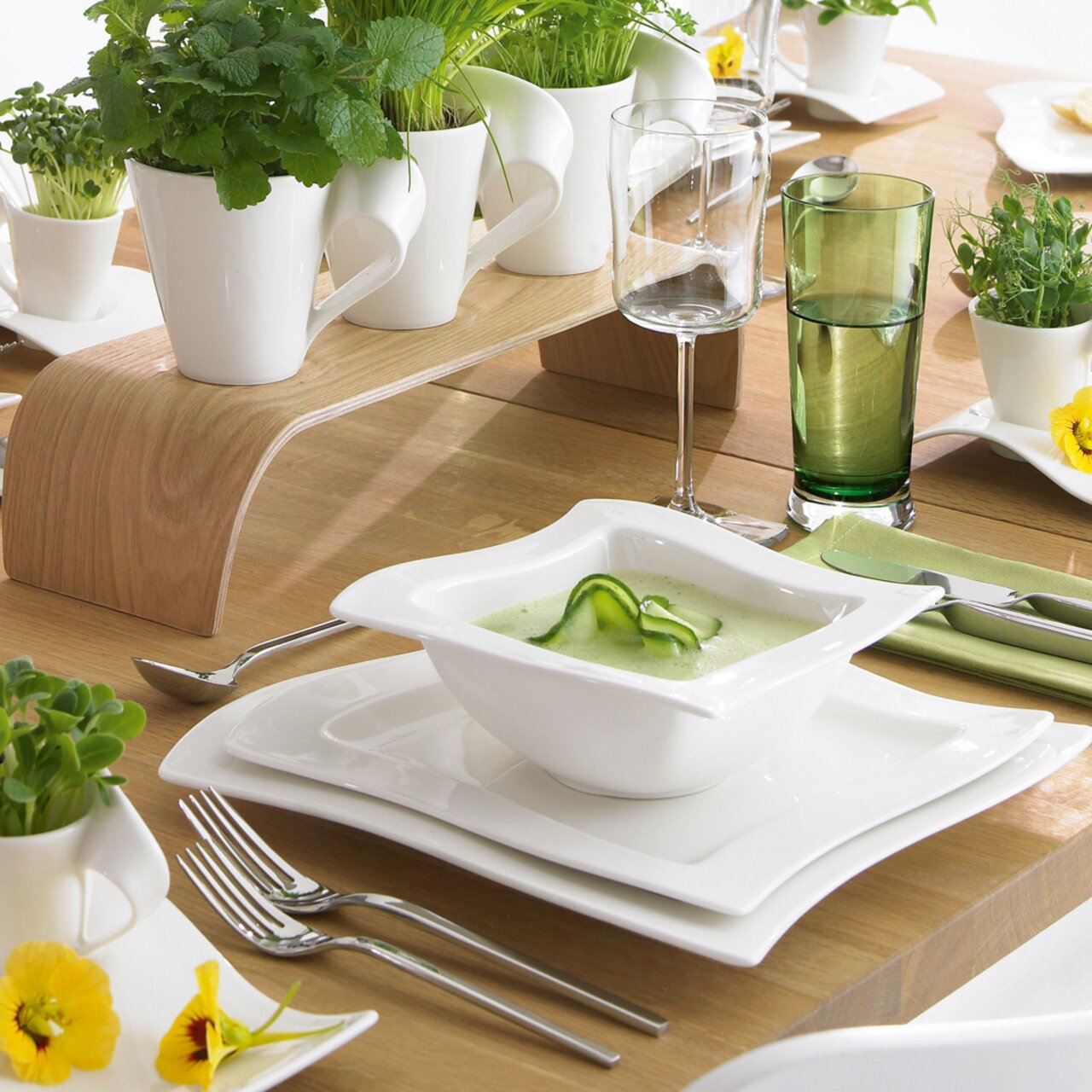 Een elegante witte kom uit de NewWave-collectie, gevuld met groene soep, op een gedekte tafel met een moderne tafeldecoratie, gezien vanuit vogelperspectief.