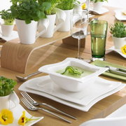 Een elegante witte kom uit de NewWave-collectie, gevuld met groene soep, op een gedekte tafel met een moderne tafeldecoratie, gezien vanuit vogelperspectief.