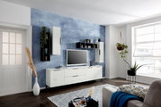 Wohnzimmeransicht mit modernem TV-Lowboard und Hängeschränken in hellem Holzdesign vor einer blauen Akzentwand, seitliche Perspektive.