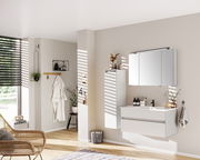 Moderne Badezimmermöbel in heller, minimalistischer Einrichtung, mit einem hängenden Waschtisch und Spiegelschrank, seitliche Perspektive.