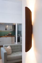 Seitliche Ansicht einer LED-Wandleuchte mit Holzoptik, die warmes Licht an die Wand strahlt.