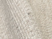Nahaufnahme eines handgewebten Teppichs in cremefarbenen Tönen, die Textur und Webart sind deutlich sichtbar.