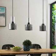 Moderne Hängeleuchte mit drei zylindrischen, rauchgrauen Glasschirmen über einem Esstisch, seitliche Perspektive.