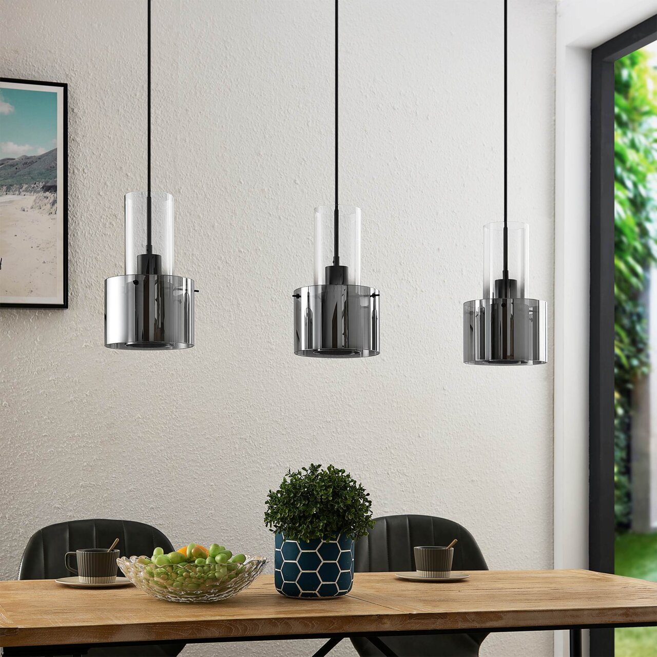 Moderne hanglamp met drie cilindervormige, rookgrijze glazen kappen boven een eettafel, gezien vanaf de zijkant.