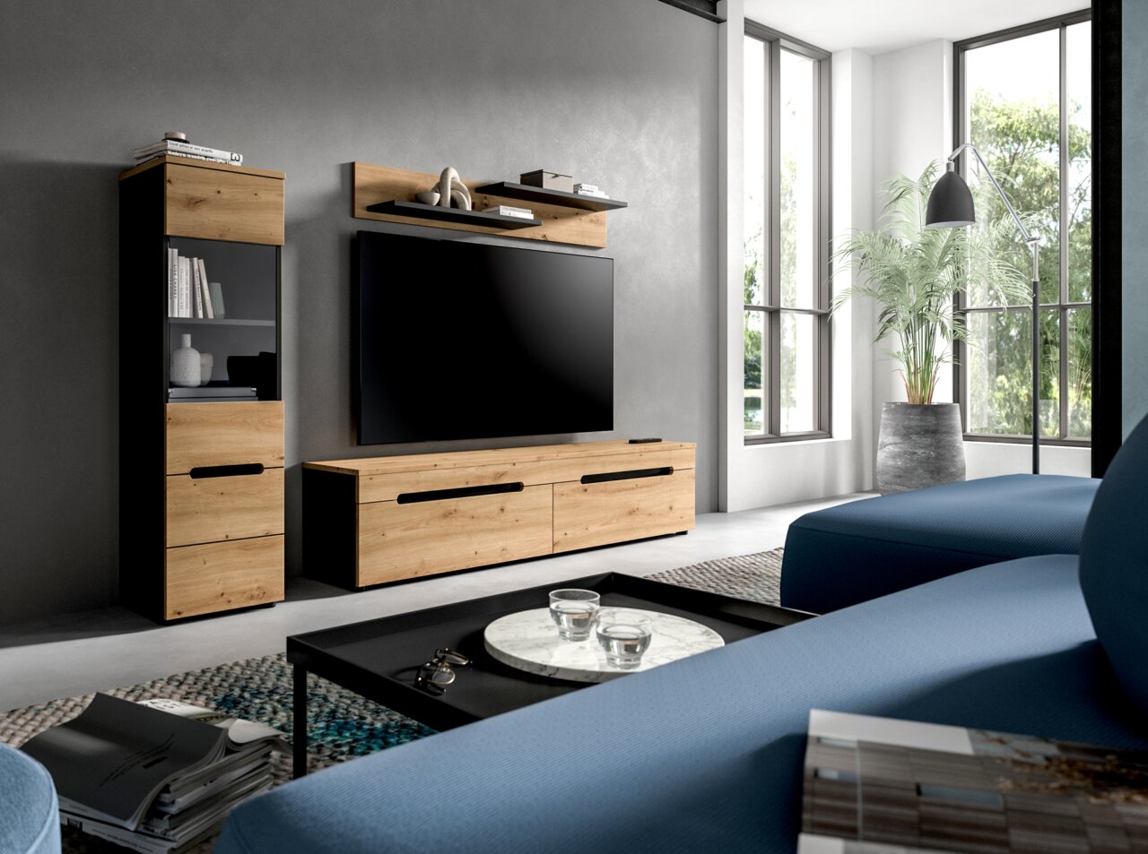 Modernes Wohnzimmer-Setup mit TV-Wandmöbeln in Holzoptik und schwarzen Akzenten (Lowboard, Hängeregal, Vitrine) vor grauer Wand, fotografiert aus schräger Frontperspektive.