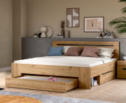 Modernes Holzbett in Eiche-Optik mit hohem Kopfteil und integrierten Schubladen/Stauraum, eine Schublade vorne ausgezogen; Ansicht schräg von vorn im Schlafzimmer-Setting.