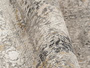 Nahaufnahme eines Designer-Teppichs mit abstraktem Muster in Grau- und Beigetönen, teilweise aufgerollt.