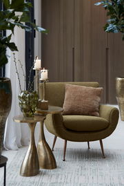 Moderner Beistelltisch mit goldener Oberfläche, dekoriert mit einer grünen Vase und Kerzen, neben einem olivgrünen Sessel. Perspektive: seitlich.