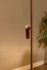 Detailaufnahme einer schlanken Stehleuchte in Bronze/Kupferoptik mit zylindrischem Schalter am Ständer, seitliche Perspektive vor beiger Wand