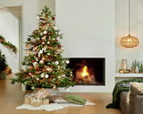 Weihnachtlich geschmückter Grandis Tannenbaum mit Kugeln und Lichtern, im Wohnzimmer neben einem Kamin, aus frontaler Perspektive.