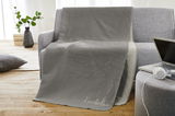 Graue Kuscheldecke auf einem Sofa drapiert, mit einem Laptop und Kopfhörern auf einem Beistelltisch in der Nähe, aus einer frontalen Perspektive fotografiert.
